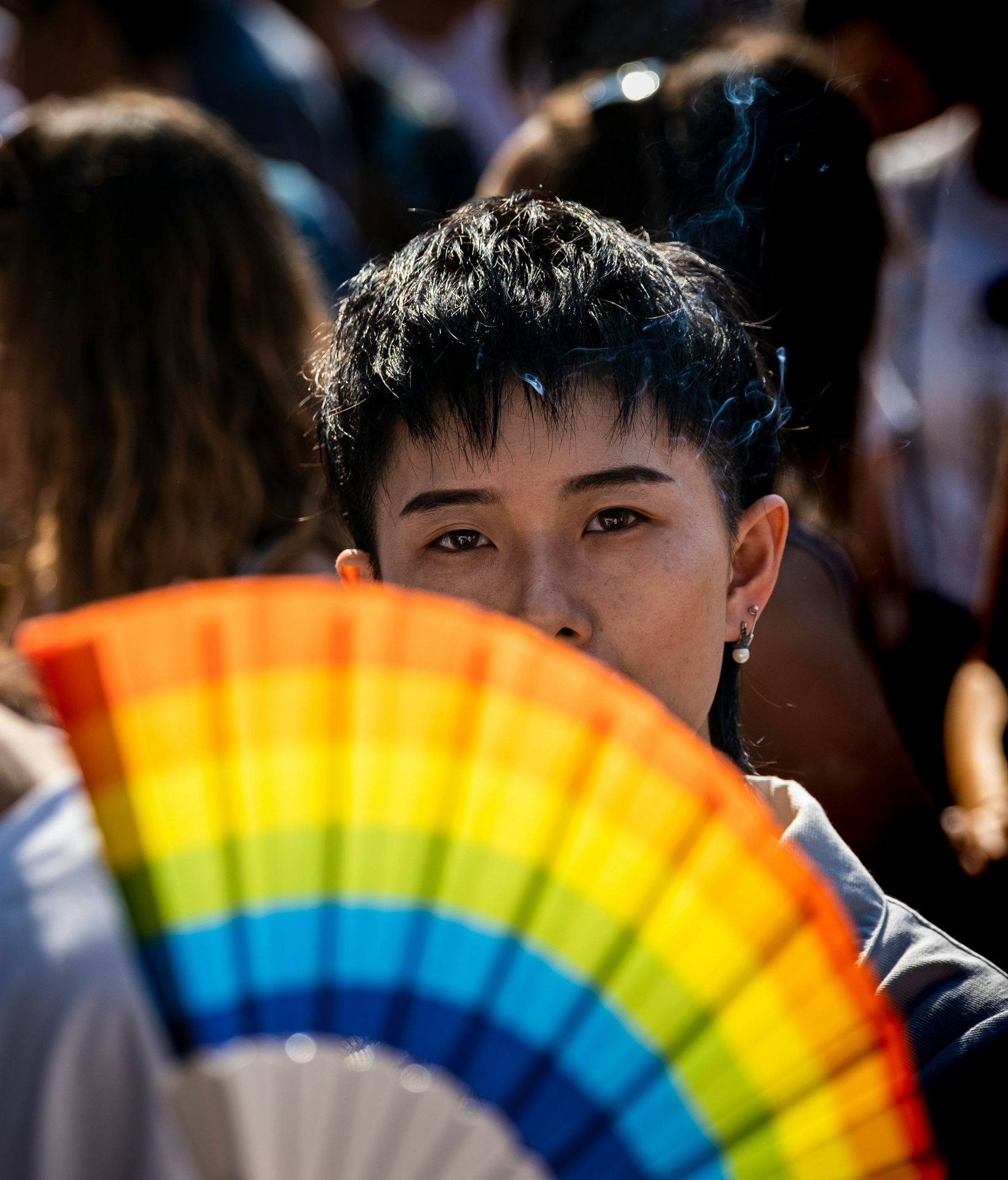Dark-haired person behind rainbow fan
