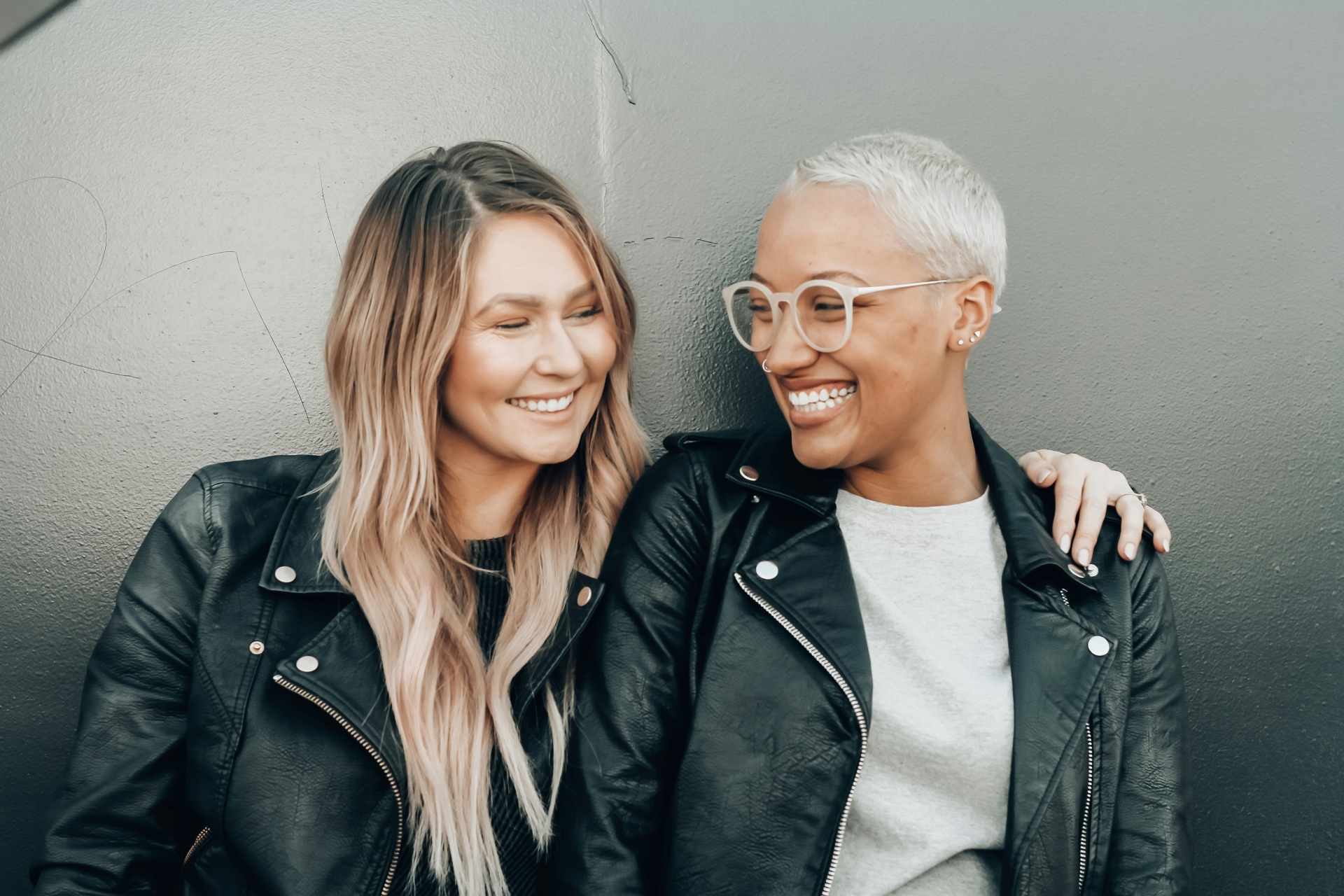 Two girls in leather coats smiling and hugging