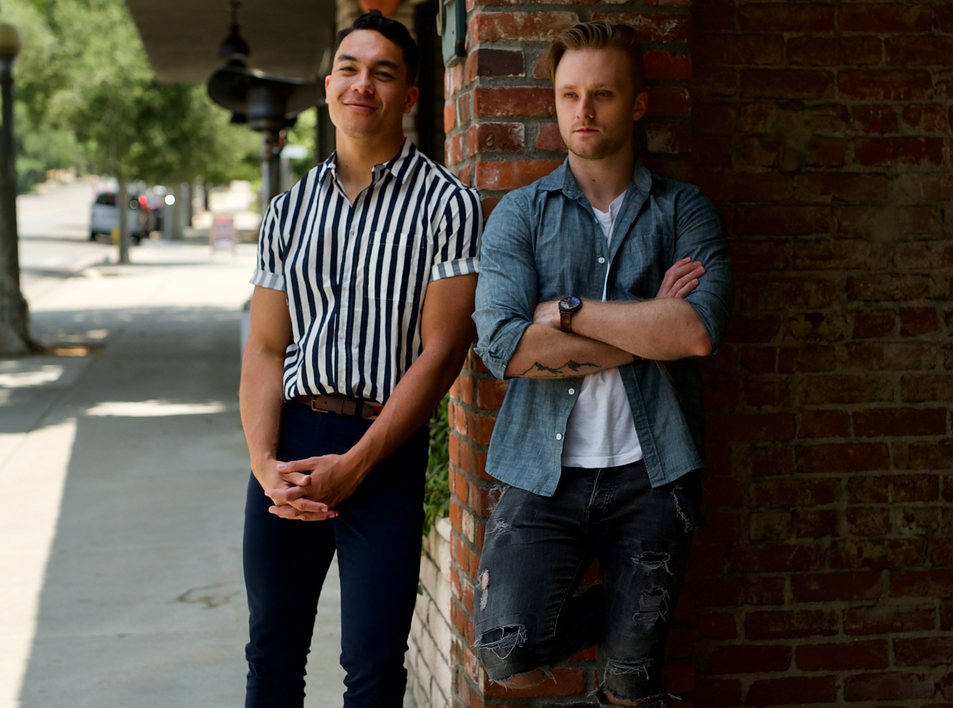 Two guys standing next to each other, leaned against a brick wall corner